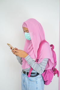 Midsection of woman with umbrella standing against pink background