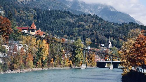 Bridge over river by buildings against trees during autumn