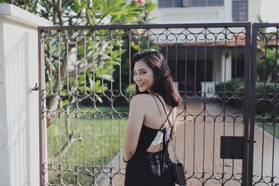 Portrait of young woman standing against fence