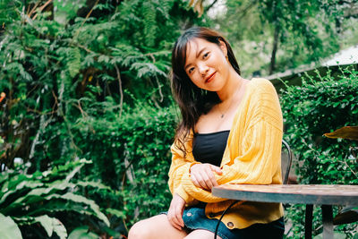 Portrait of a smiling young woman sitting against plants