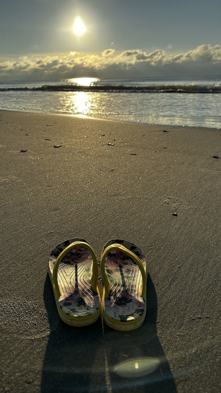 beach, land, water, sea, sky, sand, nature, sunlight, morning, beauty in nature, tranquility, scenics - nature, cloud, yellow, horizon over water, reflection, shoe, horizon, tranquil scene, outdoors, ocean, sandal, no people, pair, vacation, absence, trip, wave, sun, travel destinations, holiday, travel, flip-flops, idyllic, day
