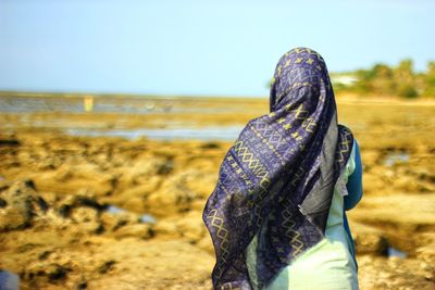 Rear view of woman wearing headscarf standing at beach against sky