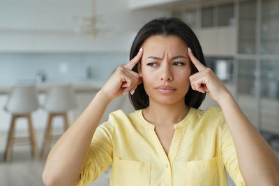 Serious woman keeps index fingers on temples, suffering from headache