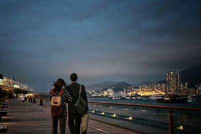 Rear view of couple looking at river against illuminated structures