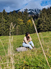Young woman sitting on grass, meadow, forest, trees, valley, autumn, fall.