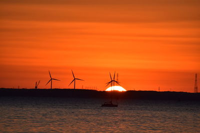 Silhouette of wind turbines in sea against sky during sunset