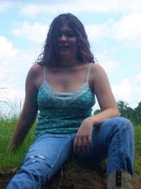 Young woman looking away while sitting on land against sky