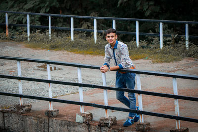 Portrait of smiling young man standing by railing outdoors