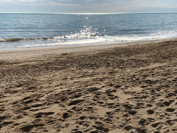 Footprints on sand at beach against sky