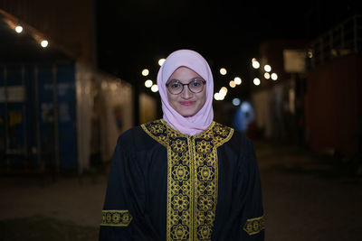 Smiling young woman wearing mortar board while standing against sky at night