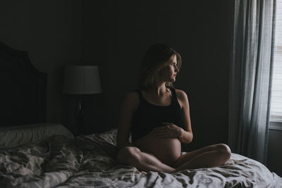 Pregnant woman looking away while sitting on bed at home