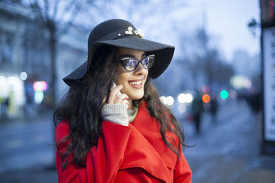 Young woman in warm clothing talking on mobile phone while standing on city street