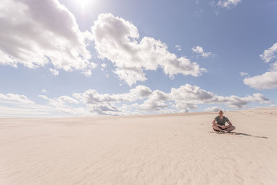 Man sitting on sand dune in desert against sky