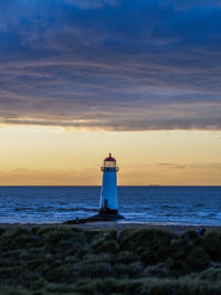 Lighthouse by sea against sky during sunset