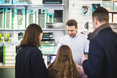 Salesman showing computer equipment to customers in electronics store