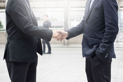 Midsection of businessman and colleague shaking hands in city