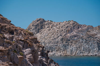 Rock formations by sea against clear sky