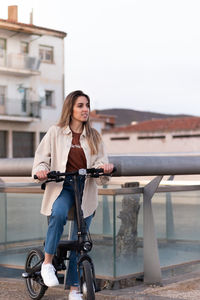 Young blonde woman sightseeing around the city with an electric bike in europe wearing casual outfit