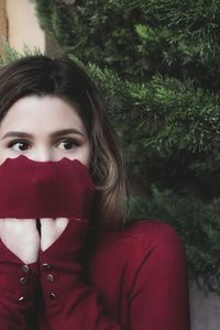 Close-up of shocked woman covering face with sweater against tree