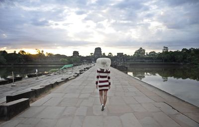 Rear view of woman walking on footpath amidst lake during sunset