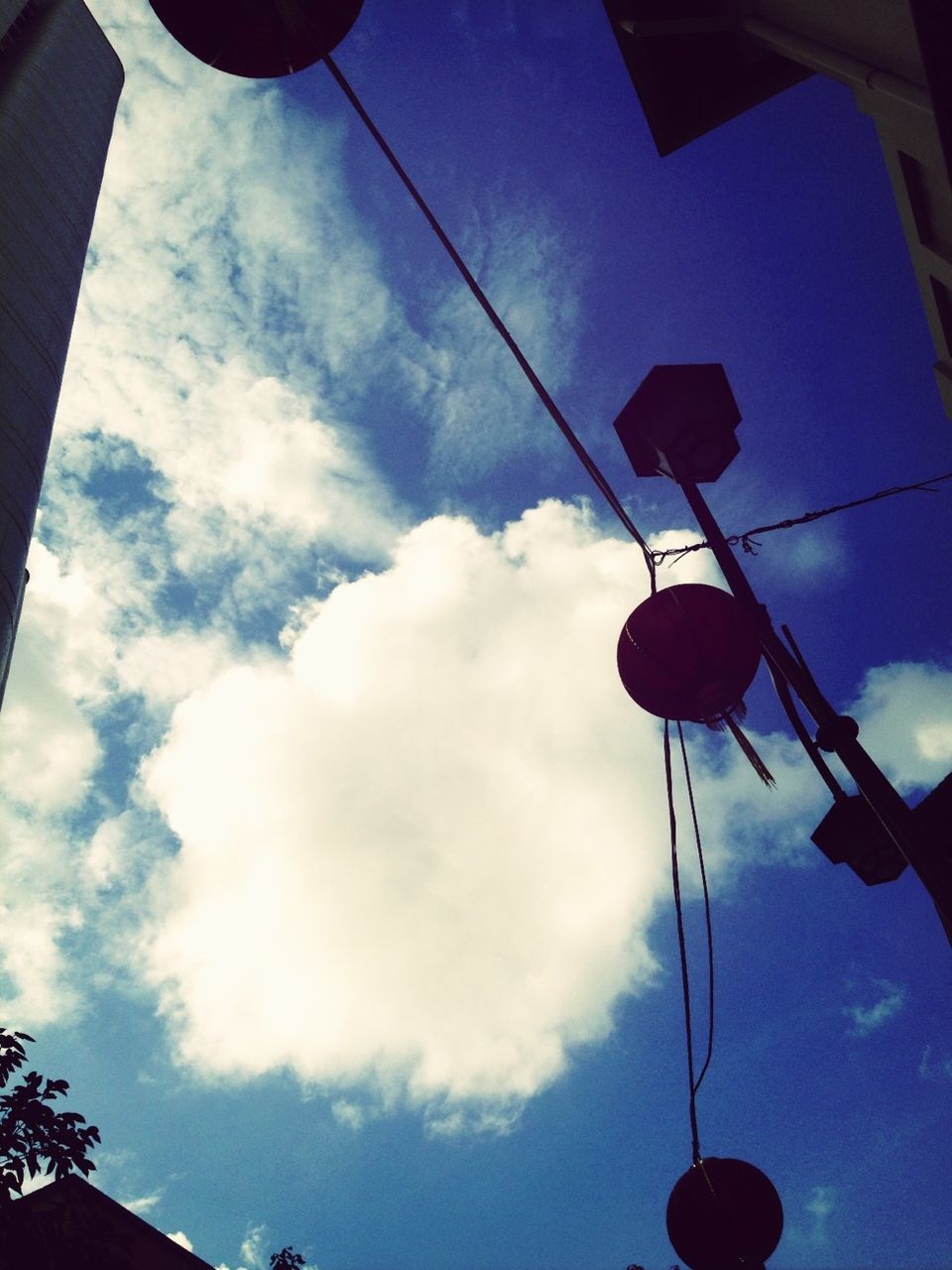 low angle view, lighting equipment, sky, street light, electricity, hanging, built structure, cable, architecture, power line, cloud - sky, electric light, building exterior, lantern, illuminated, cloud, silhouette, blue, no people, outdoors