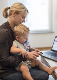 Mother with baby boy using mobile phone at home