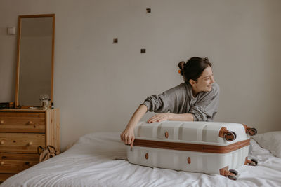 Smiling woman packing her suitcase at home on the white bed