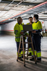 Group of skilled male engineers in uniform using gadgets while examining electrical equipment in modern building