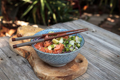 Raw salmon poke bowl with rice, cabbage, cucumber, sesame seeds and spring rolls with chopsticks.