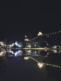 Illuminated bridge over river against sky at night