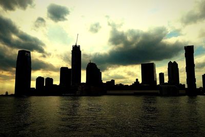 Silhouette buildings by river against sky during sunset