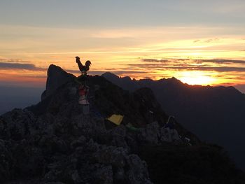 Silhouette person on rock against sky during sunset