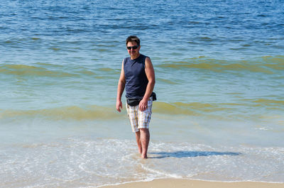 Portrait of man wearing sunglasses while standing on shore at beach