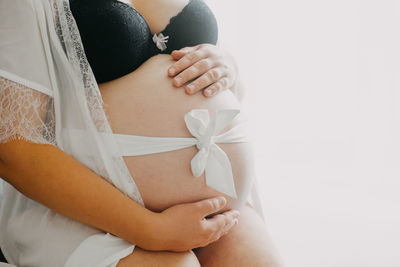 Midsection of pregnant woman measuring abdomen while standing against white background