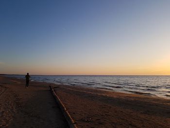 Person standing at beach against clear sky during sunset