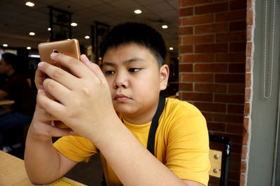 Boy using mobile phone while sitting in cafe