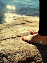 Low section of woman standing on rock by lake during sunset