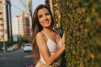 Smiling young woman standing against creeper wall