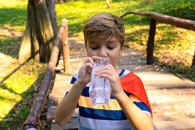 Cute boy drinking water on footbridge at park