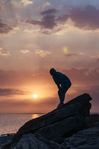 Man standing on rock by sea against sky during sunset