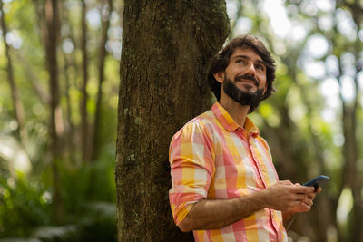 Young man with smartphone at day time with a green park in the background. mobile phone, technology,