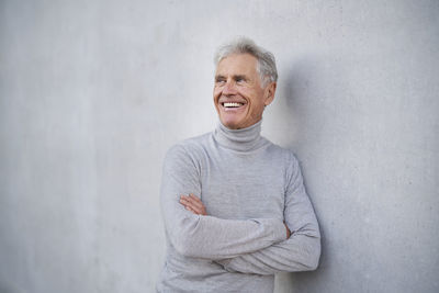 Thoughtful senior man with arms crossed by wall