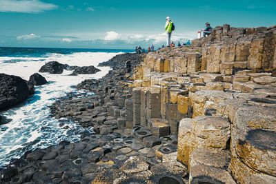 Rear view of man standing on rock by sea against sky