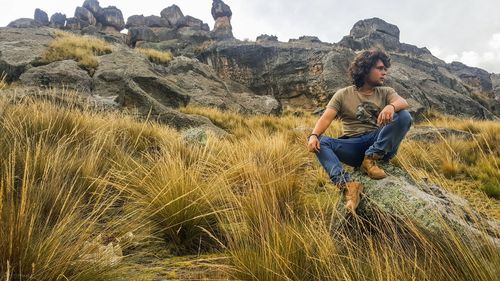 Full length of man sitting on field against sky