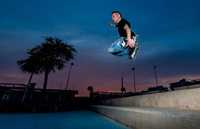 Low angle view of man jumping with inline skate against sky at dusk