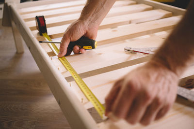 Cropped hands of man measuring wood at home