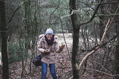 Portrait of young woman standing by bare tree in forest