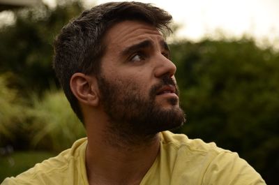 Young man looking away against trees