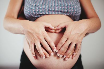 Pregnant woman and husband making heart with hands over abdomen against white background