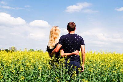Rear view of couple standing amidst yellow flowers on oilseed rape field